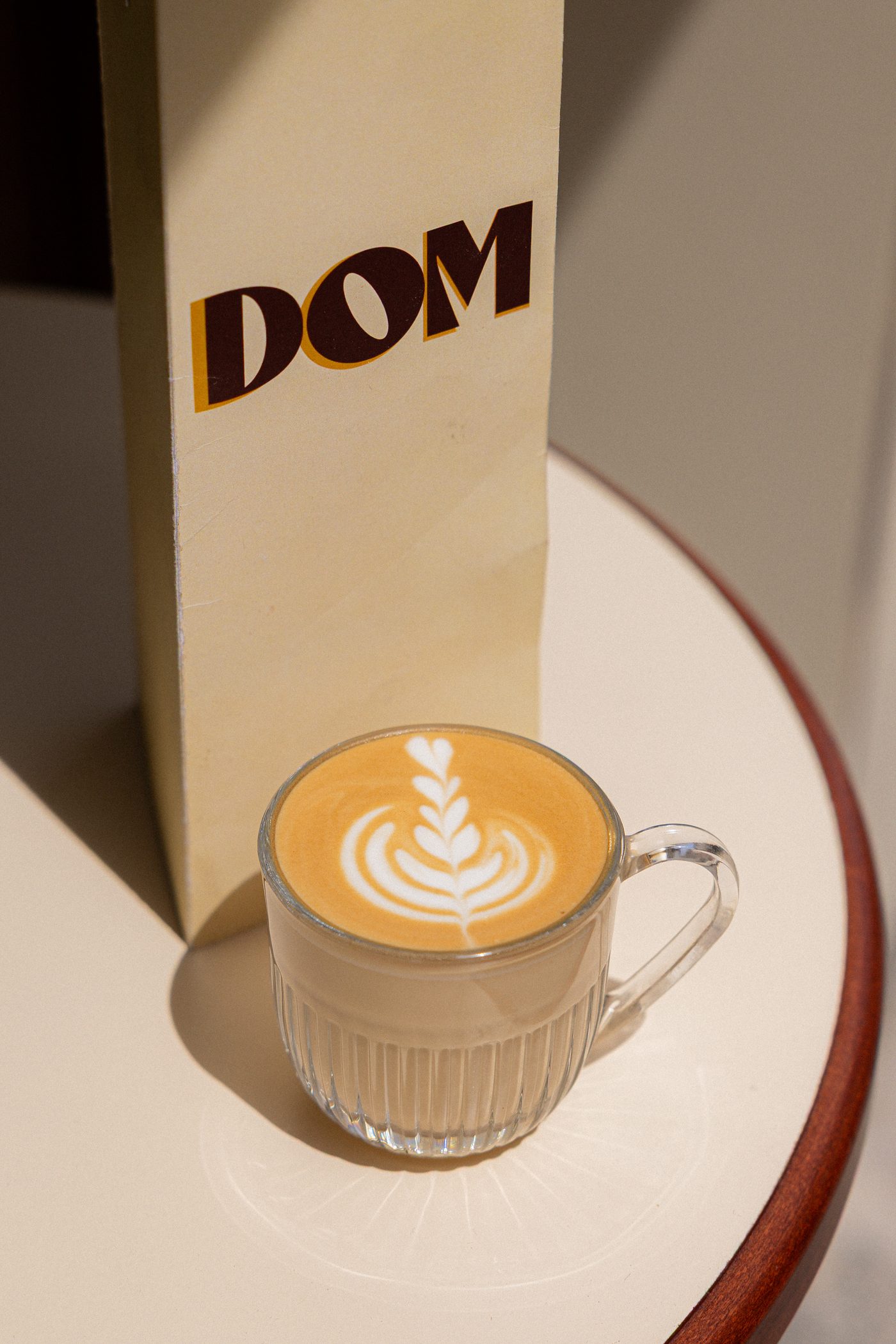 Latte art réalisé à la main chez DOM, servi dans une tasse en verre côtelée